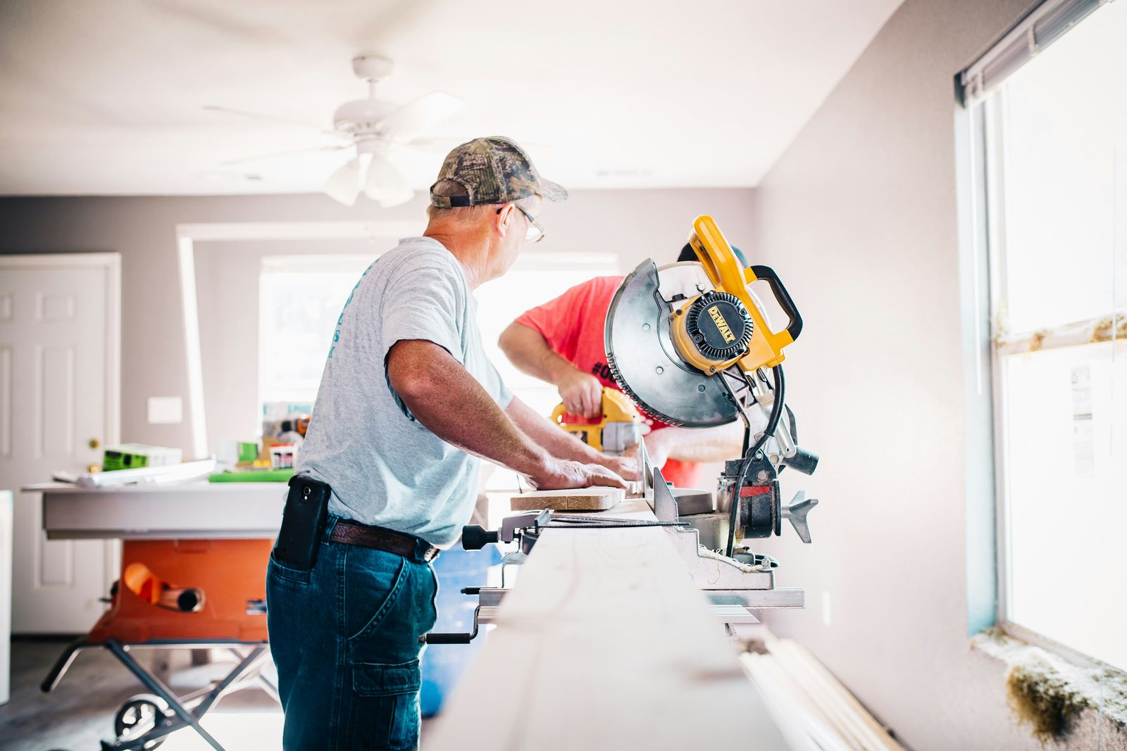 Carpenter cutting trim on a miter saw inside a room under renovation