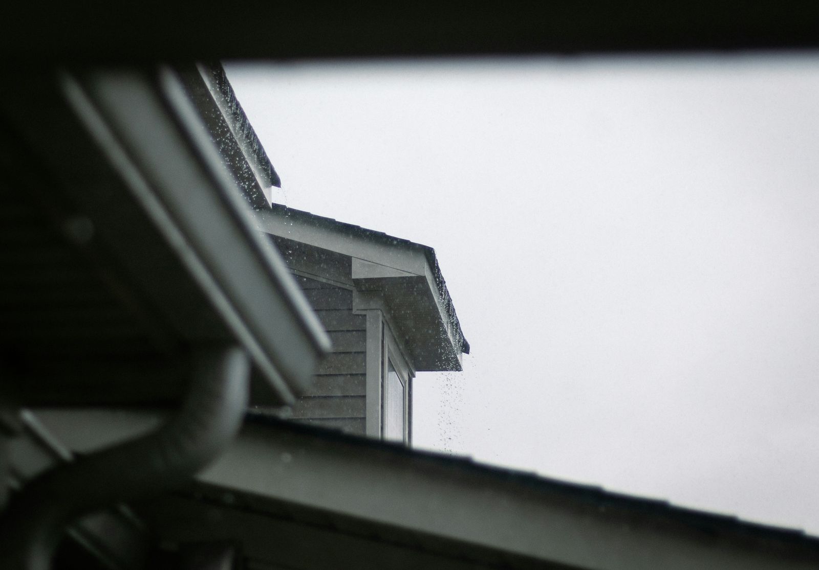 Gutter running along the edge of a shingle roof against a clear sky