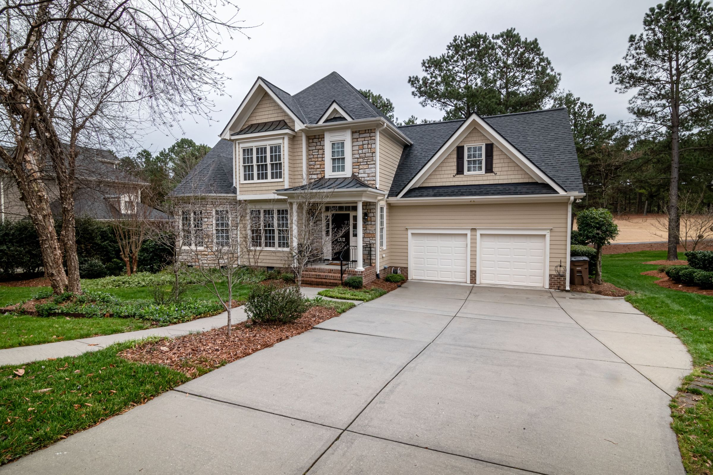 Two-story home with a shingle roof and siding, seen from the driveway on an overcast day