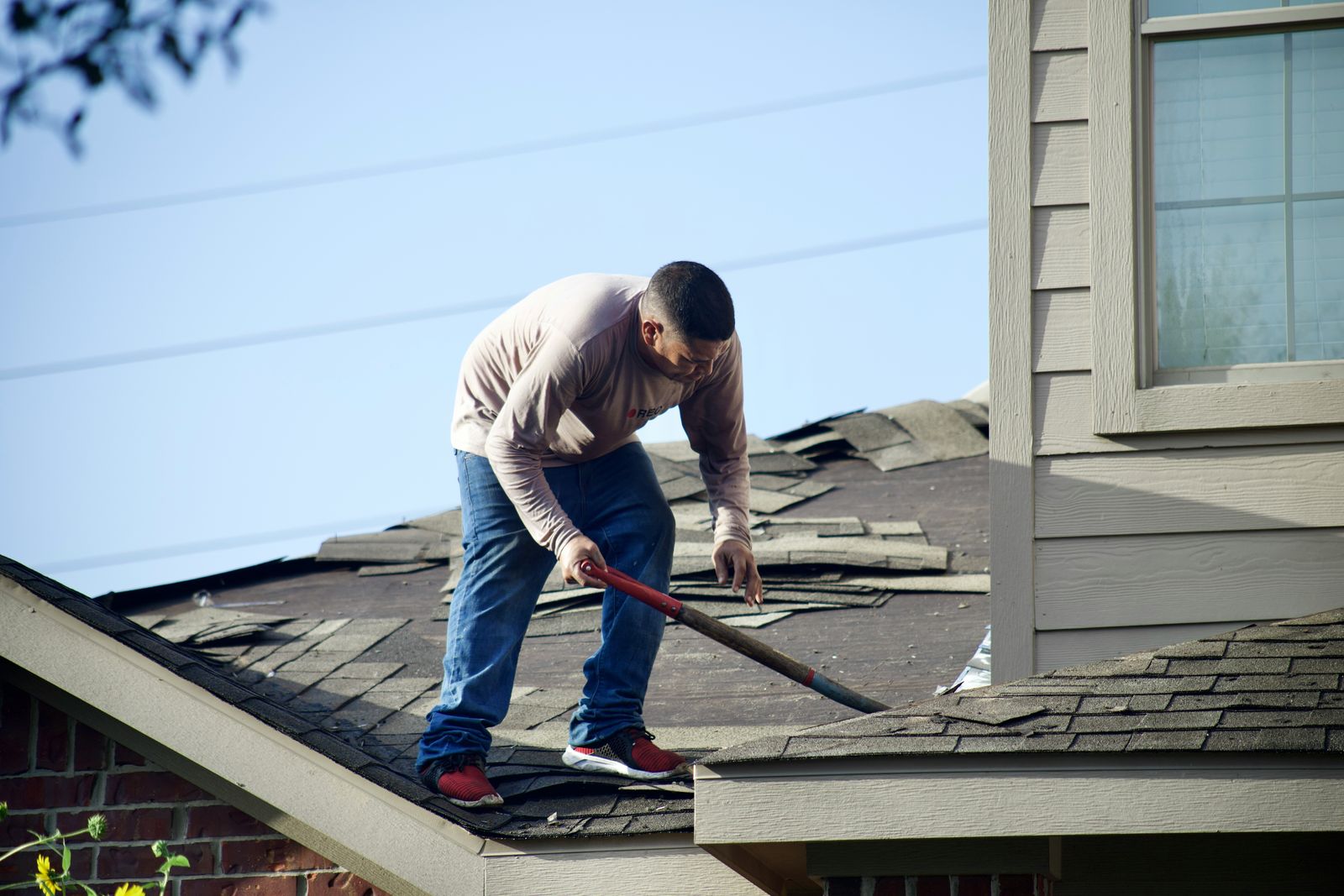 Roofer stripping old shingles off a house before a replacement roof goes on